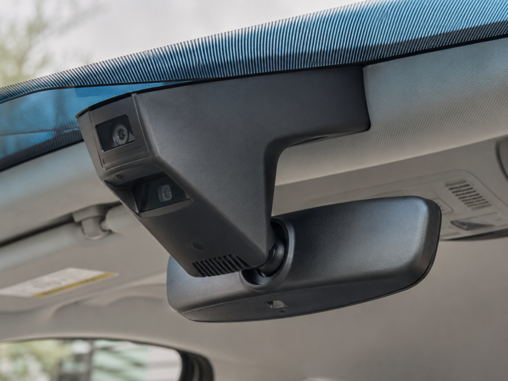 Close-up of a black dash cam mounted on the windshield above the rearview mirror inside a car.
