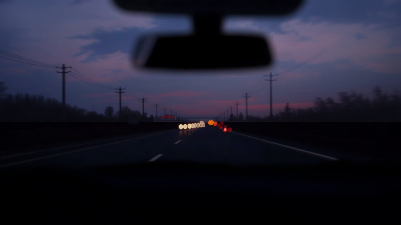 View through a windshield from the driver's seat showing a faint head-up display readout above a blurred highway at dusk
